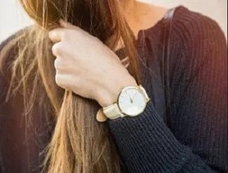 A woman wearing a wristwatch, with her hand touching her hair